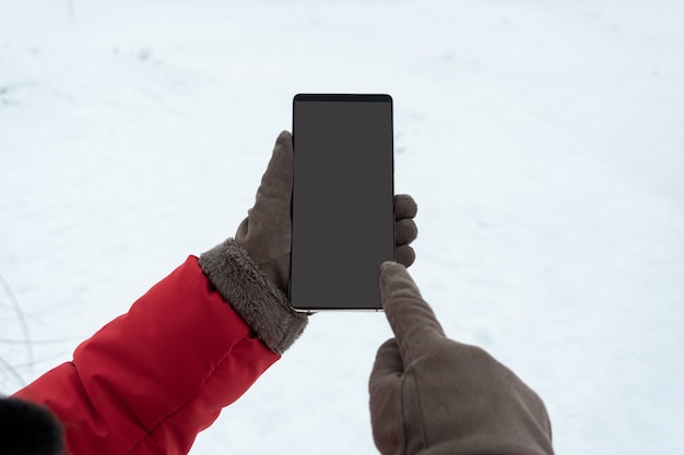 Mano femenina en guantes de invierno tocando el teléfono inteligente con pantalla en blanco