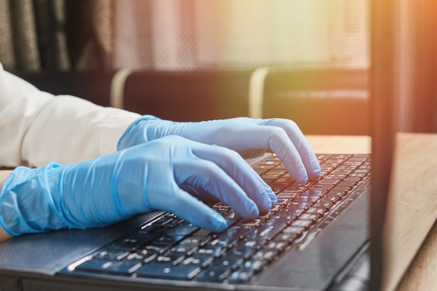 Mano femenina en guantes protectores escribiendo en el teclado del ordenador portátil. Protección contra coronavirus covid-19 en lugares públicos.