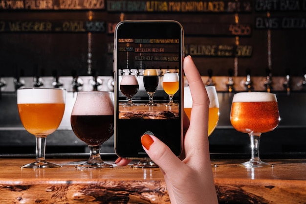 Mano femenina haciendo una foto de diferentes tipos de cerveza artesanal en vasos