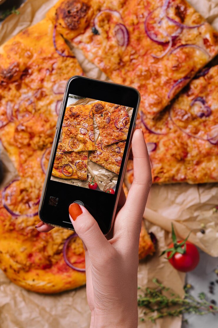 Mano femenina haciendo una foto de pizza con un teléfono móvil