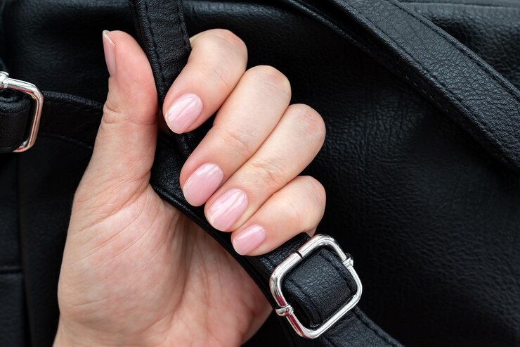 Mano femenina con hermosa manicura uñas rosa nude con mochila de cuero ecológico negro primer plano