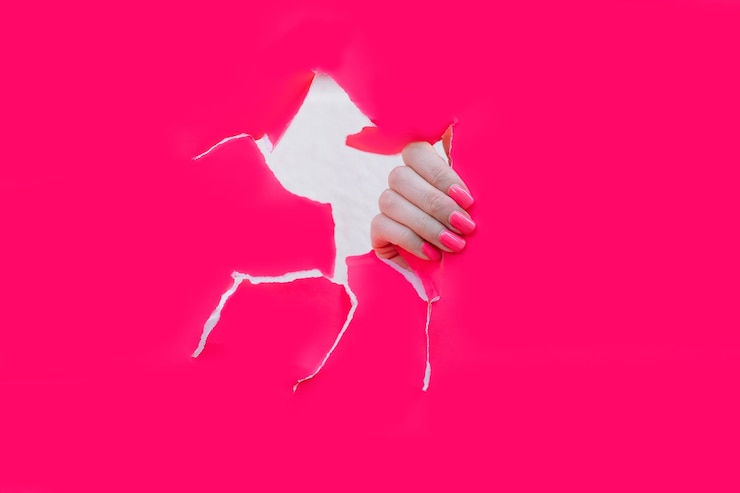 Foto mano femenina con hermosas uñas con manicura rosa en agujero de papel rosa