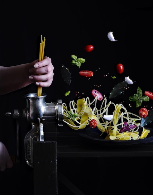 Foto la mano femenina inserta pasta seca en una picadora de carne y, a la salida, pasta hervida. arte digital