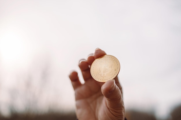 Mano femenina irreconocible que muestra la moneda en efectivo de bitcoin con espacio de copia sobre fondo de cielo