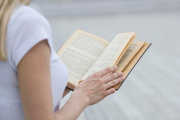 Mano femenina joven que sostiene un libro viejo - leyendo al aire libre, de cerca