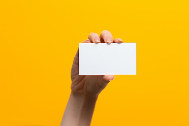 Mano femenina levantada con una tarjeta blanca. Bosquejo. Fondo amarillo. Copie el espacio.