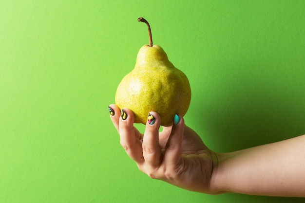 Mano femenina con manicura colorida con pera sobre fondo verde