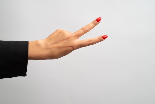 Mano femenina con manicura roja muestra gesto sobre fondo blanco.