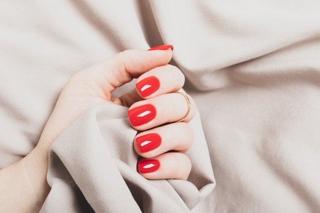 Mano femenina con manicura rojo brillante sobre un fondo de tela beige