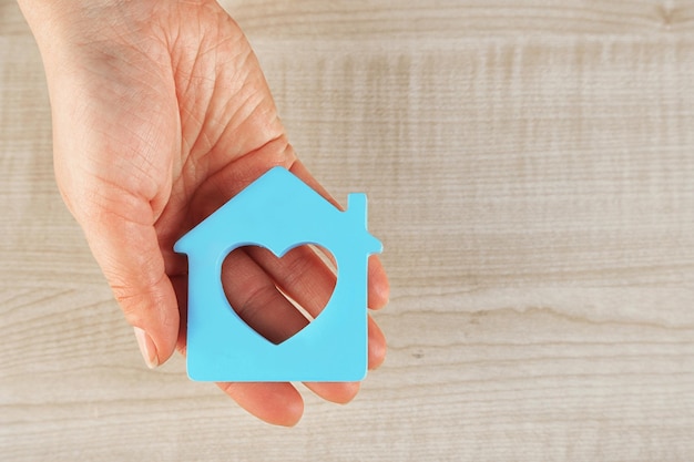 Mano femenina con modelo de casa sobre fondo de mesa de madera