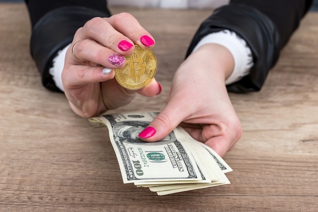 Mano femenina mostrando bitcoin y mantenga billetes de dólar