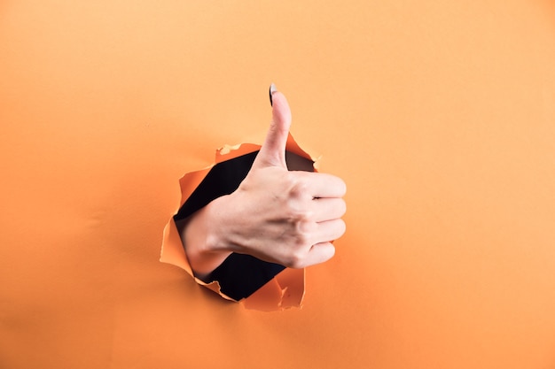 Mano femenina mostrando el pulgar hacia arriba sobre fondo naranja