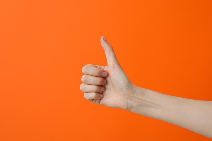 Mano femenina mostrando el pulgar hacia arriba sobre fondo naranja