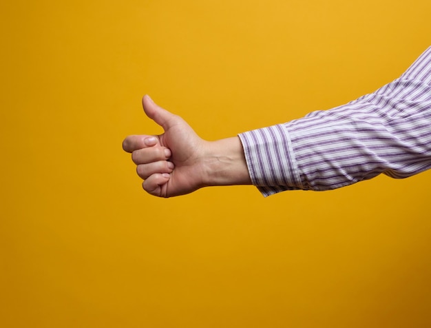 La mano femenina muestra como gesto sobre fondo amarillo. Concepto de aprobación