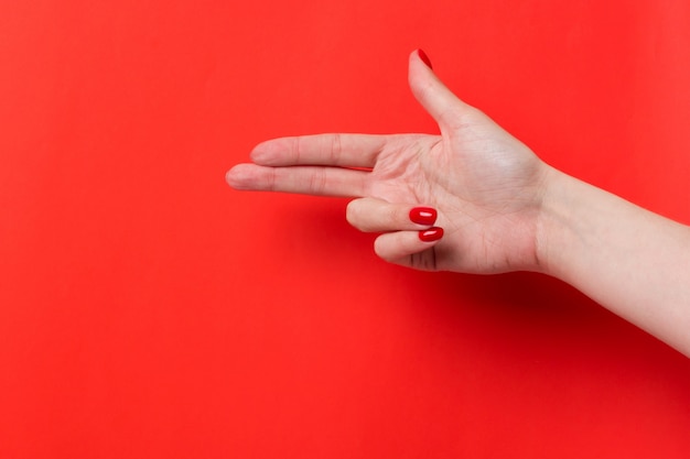 La mano femenina muestra un gesto de signo de arma sobre un fondo rojo. Lugar para texto