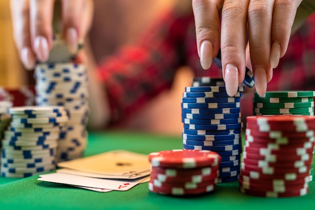 Mano femenina con naipes y fichas de póquer de cerca frente a la mesa de póquer