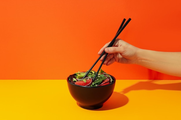 Mano femenina con palillos y ensalada con naranja roja