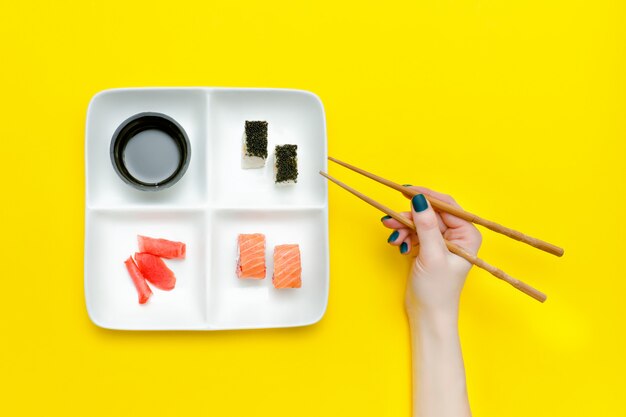 Mano femenina con palillos y plato con sushi