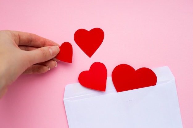 La mano femenina pone corazones rojos de papel en un sobre blanco. Mensaje de amor. Concepto de San Valentín