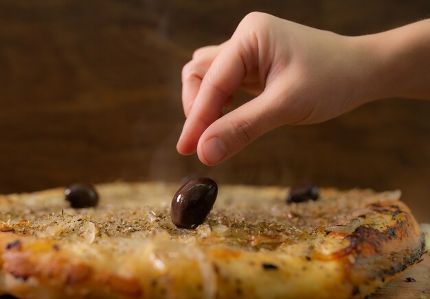 Foto mano femenina poniendo una aceituna negra en una pizza