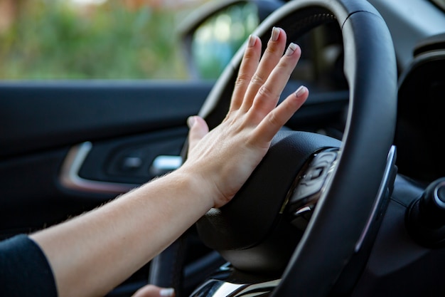 Mano femenina presiona la bocina en el volante de un automóvil moderno. no cara