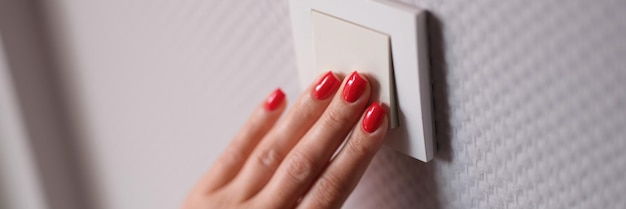 La mano femenina presiona el interruptor blanco en el primer plano de la pared gris