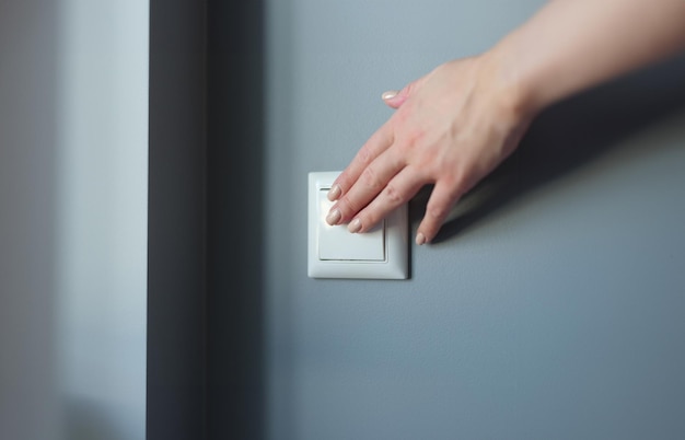 Mano femenina presionando el interruptor de luz en el apartamento closeup
