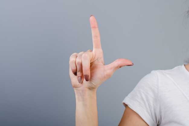 Mano femenina en puño mostrando dos dedos aislados sobre gris