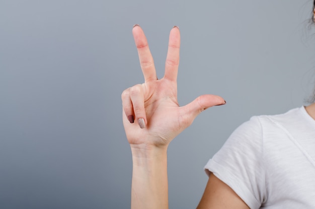 Foto mano femenina en puño mostrando tres dedos aislados sobre gris