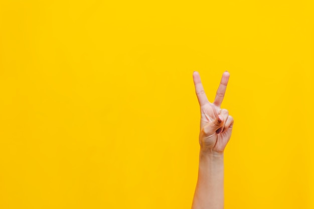 Mano femenina que muestra un gesto de paz aislado en una pared de color amarillo brillante