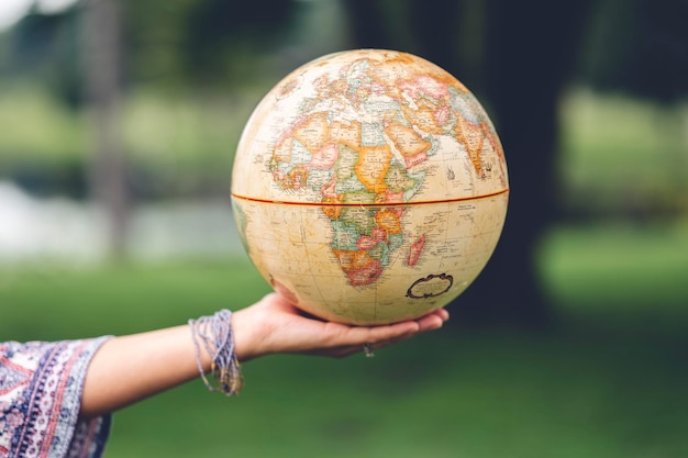 Mano femenina que presenta un globo vintage en el fondo borroso, viaja y explora el mundo