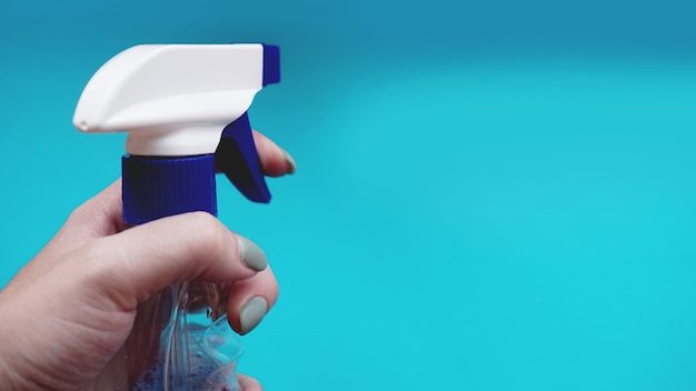 Mano femenina que sostiene el aerosol con detergente sobre fondo azul. Concepto de tareas domésticas, limpieza y hogar