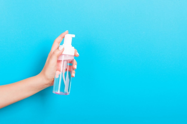 Mano femenina que sostiene la botella de la crema del aerosol de loción aislada. Chica dar productos cosméticos sobre fondo azul.