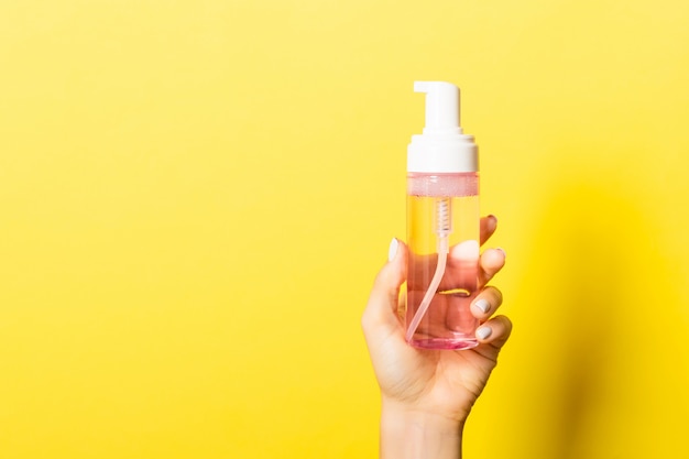 Mano femenina que sostiene la botella de la crema del aerosol de loción aislada. Chica dar productos cosméticos