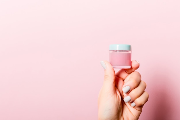 Mano femenina que sostiene la botella poner crema de loción aislada. Chica dar tarro productos cosméticos en rosa