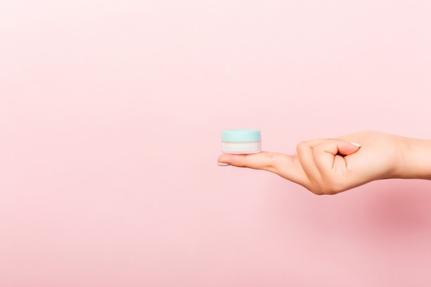 Mano femenina que sostiene la botella poner crema de loción aislada. Chica dar tarro productos cosméticos sobre fondo rosa