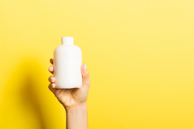 Mano femenina que sostiene la botella poner crema de loción aislada.