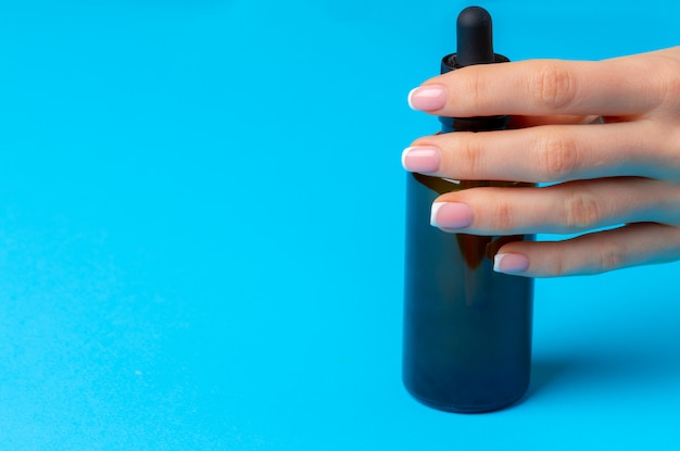 Mano femenina que sostiene la botella del producto para el cuidado de la piel en azul