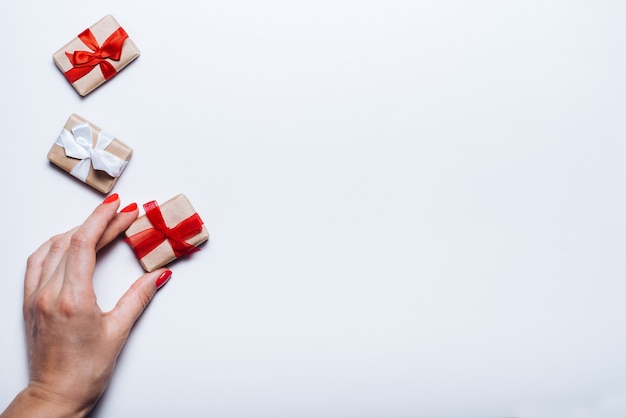 Mano femenina que sostiene la caja de regalo con cinta roja sobre fondo blanco en blanco