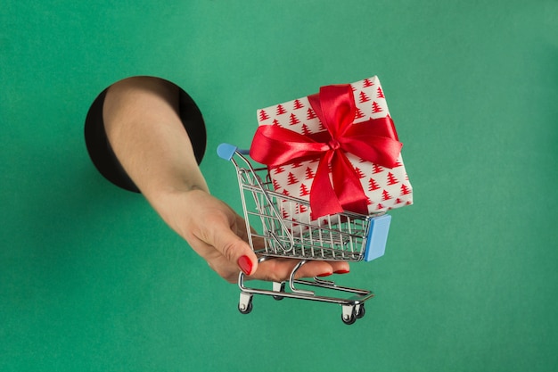 Mano femenina que sostiene la caja de regalo de navidad a través del agujero redondo en papel verde.