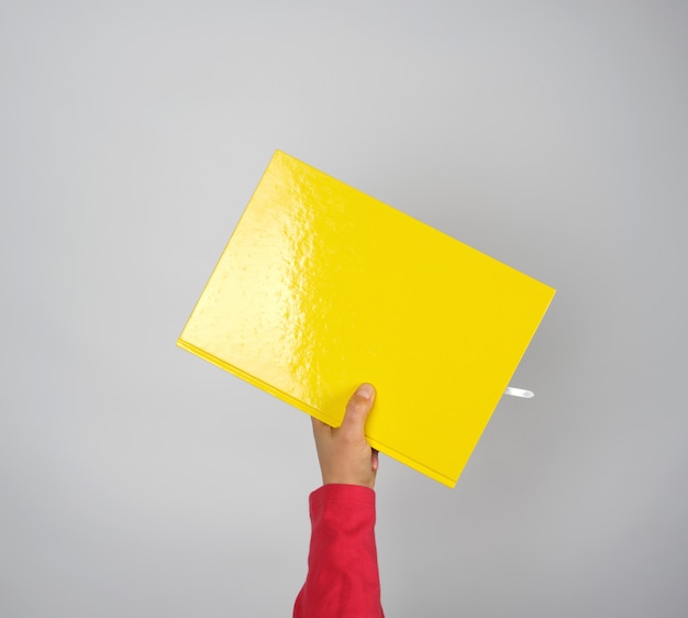 Mano femenina que sostiene un cuaderno amarillo