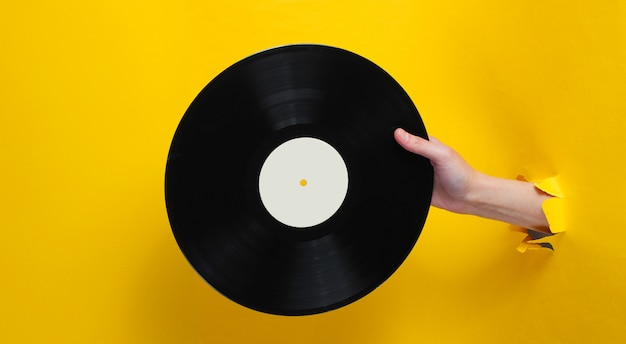 Mano femenina que sostiene el disco de vinilo a través del agujero rasgado de papel amarillo. Concepto retro minimalista