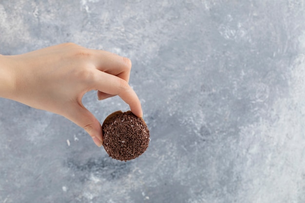 Mano femenina que sostiene la galleta fresca con chispitas de chocolate sobre la superficie de piedra