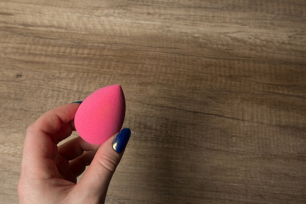 Foto mano femenina que sostiene la licuadora de belleza rosa sobre un fondo de madera. espacio vacio