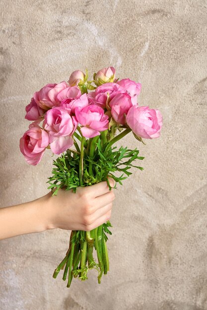 Mano femenina que sostiene el ramo de hermosas flores de ranúnculo sobre fondo de color