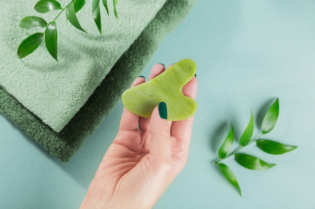 Mano femenina que sostiene el raspador del gua sha del masaje para la cara de la piedra del jade verde