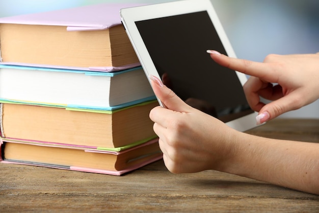 Mano femenina que sostiene la tableta de la PC cerca de libros closeup Concepto de educación moderna