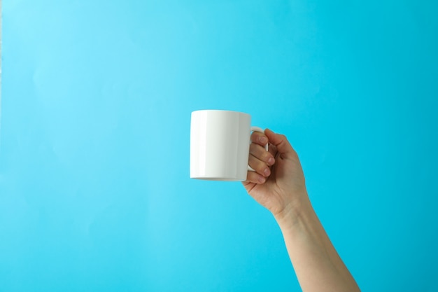 Mano femenina que sostiene la taza blanca contra fondo del color