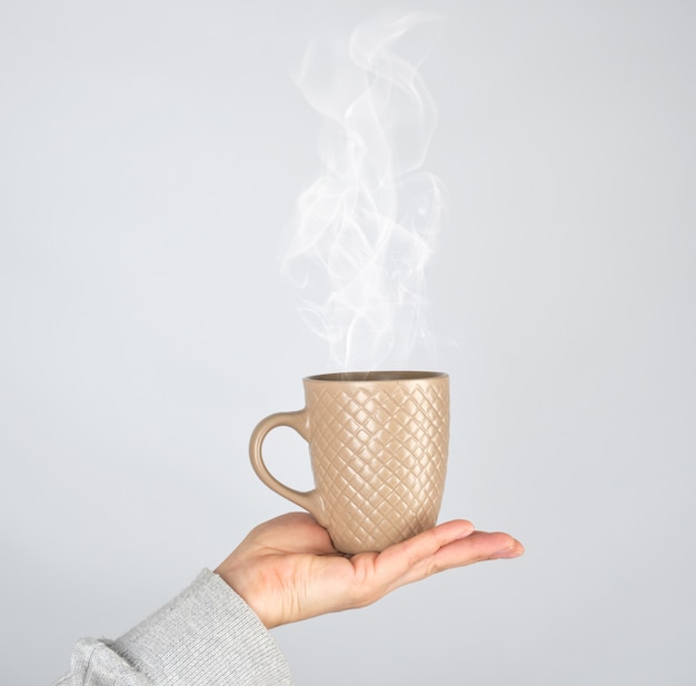 Foto mano femenina que sostiene una taza de cerámica marrón con una bebida