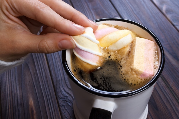 Mano femenina que sostiene la taza de chocolate o chocolate caliente con malvavisco en mesa de madera desde arriba